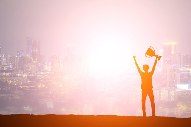 Silhouette man holding up a gold trophy cup as a winner in a competition